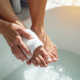 Personne agee hydrate ses pieds dans une salle de bain lumineuse